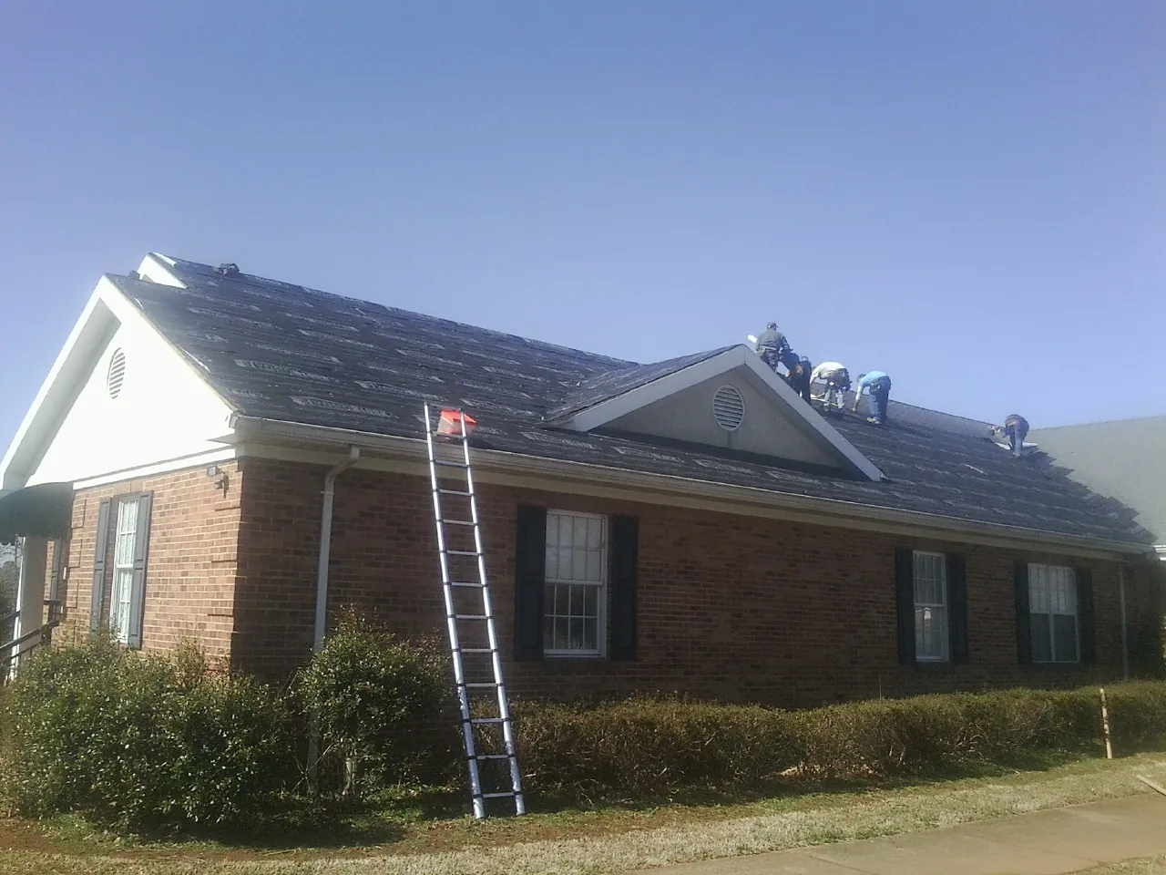 Crew tearing shingles off a brick ranch roof with a ladder set — Emergency Roof Repair work by our crew in Londonderry