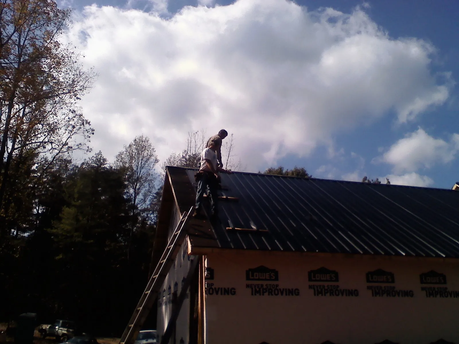 Roofer fastening dark metal panels high against a cloudy sky, from a Roof Inspection job in Londonderry