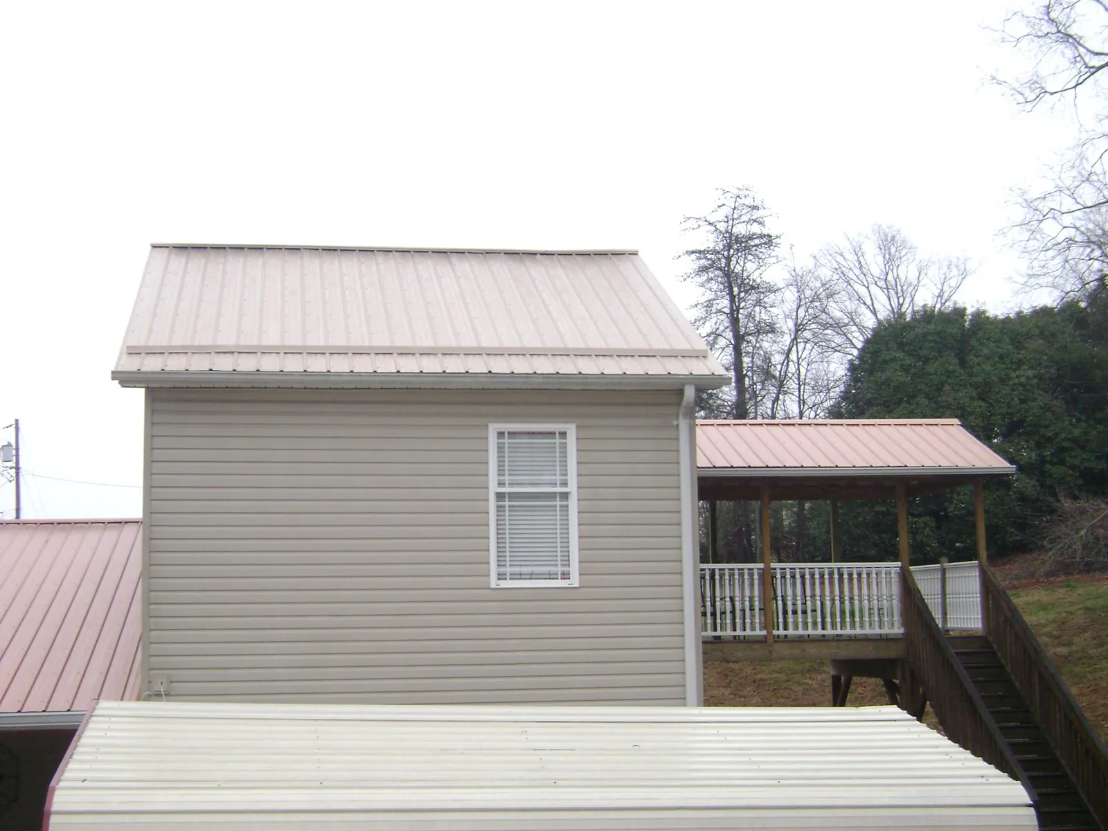 Tan metal roofs on a two story addition and attached porch, from a Roof Replacement job in Londonderry